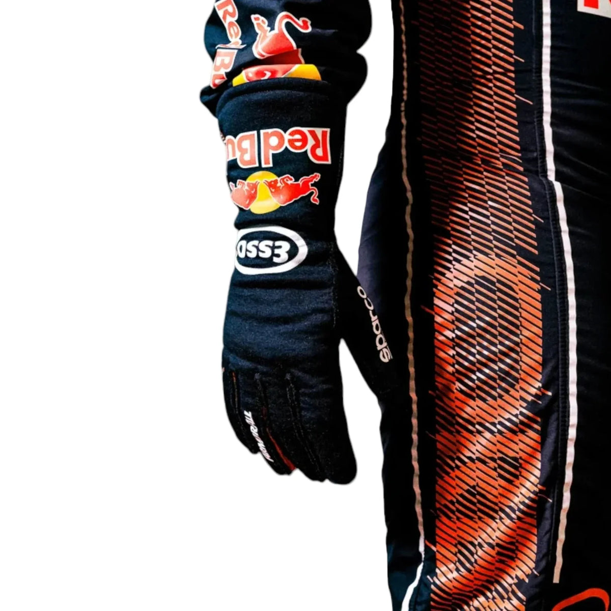 A close-up of a black racing suit or glove with Red Bull, Essor, and Cosworth branding, featuring a bold orange and white striped graphic pattern on the adjacent section, set against a plain white background.