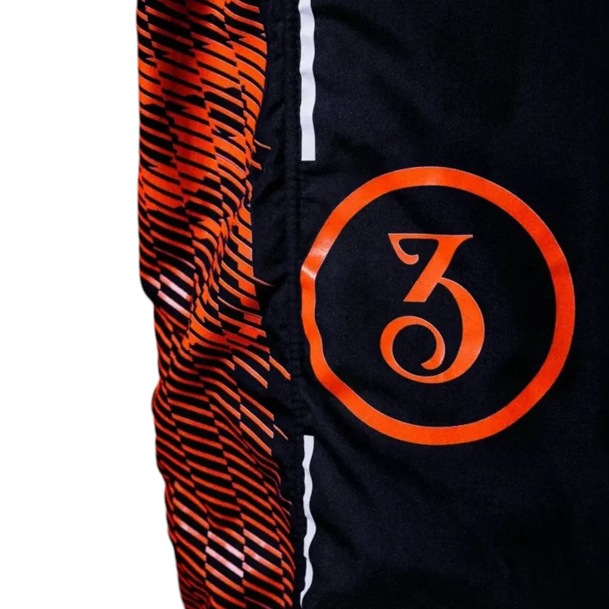 Close-up of a black athletic garment featuring a bold orange circular logo with a stylized number 3 on the side, alongside a textured orange and black patterned panel and thin white piping.