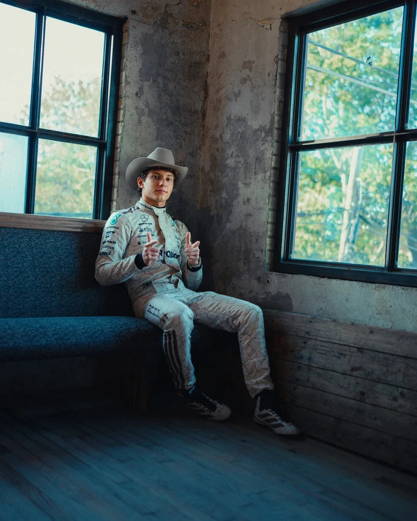 Andrea Kimi Antonelli in a cowboy hat and light-colored outfit sitting on a blue couch in a room with large windows.