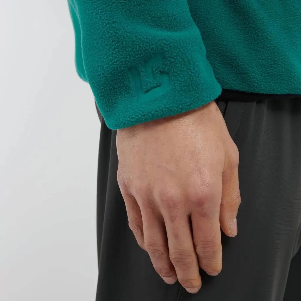 Hand wearing a green fleece sleeve against a plain background