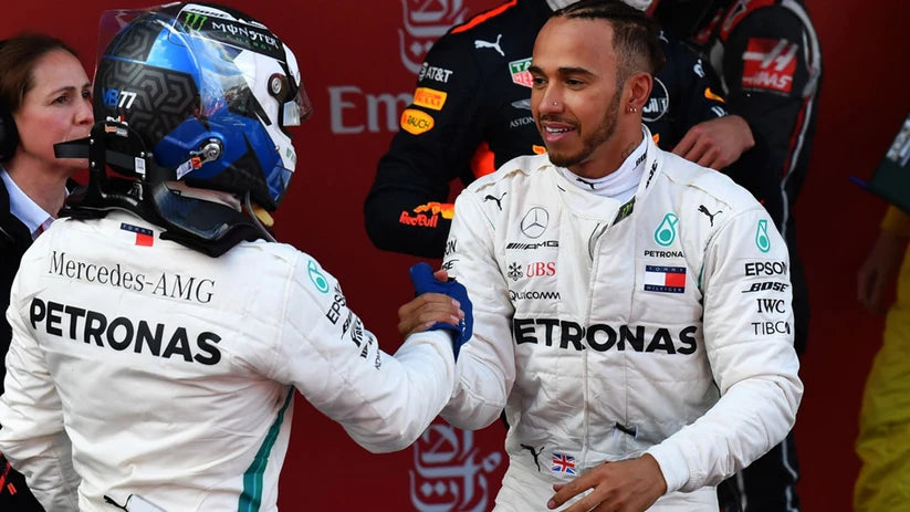 Two Formula 1 drivers in white Mercedes-AMG Petronas uniforms shaking hands on a red background.