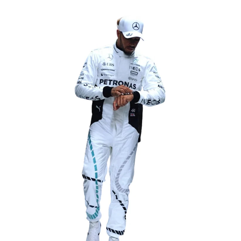 Lewis Hamilton wearing a white Mercedes racing suit and matching cap, with Petronas and other sponsor logos visible, standing against a plain white background while looking at his wristwatch.