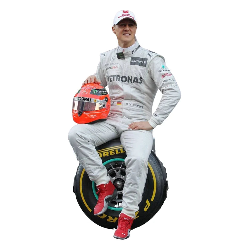 Michael Schumacher in Mercedes 2012 F1 Racing Suit and helmet sitting on a racing tire with visible branding.