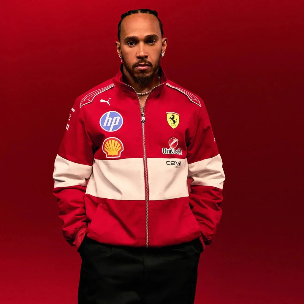Lewis Hamilton wearing a Official PUMA 2025 F1 Vintage Racing Team Jacket with various logos on a red background