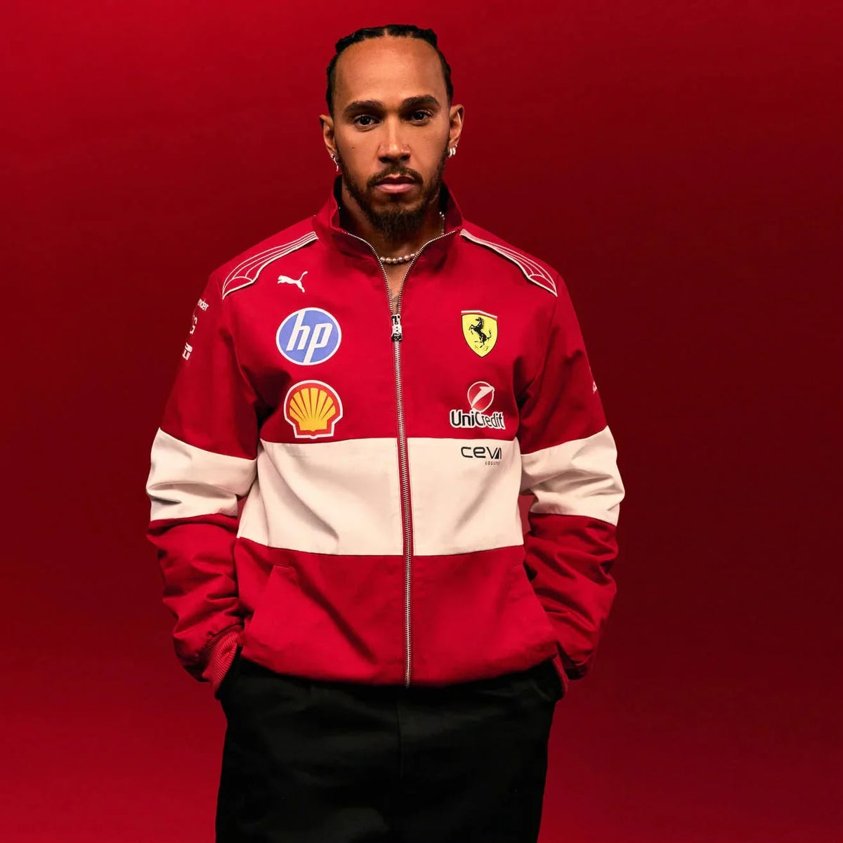 Lewis Hamilton wearing a Official PUMA 2025 F1 Vintage Racing Team Jacket with various logos on a red background