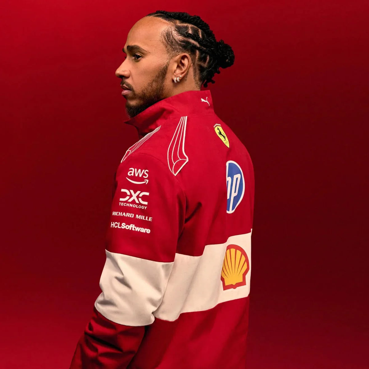 Lewis Hamilton wearing a Official PUMA 2025 F1 Vintage Racing Team Jacket with various logos on a red background side pose